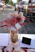 Luxury Champagne Blush Tulips floral candle arrangement displayed in an elegant gold stand at an outdoor market.